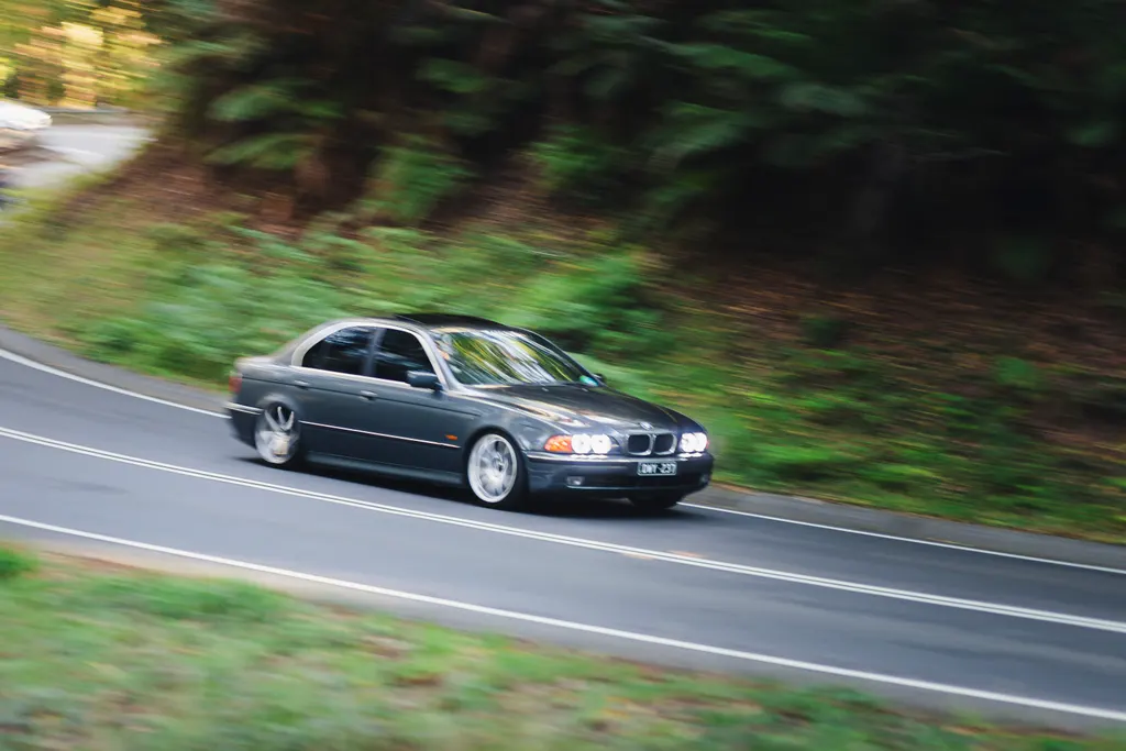 Dark sedan driving on a curved road surrounded by green forest and trees.