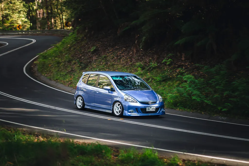 Blue hatchback navigating a winding forest road with white line markings.