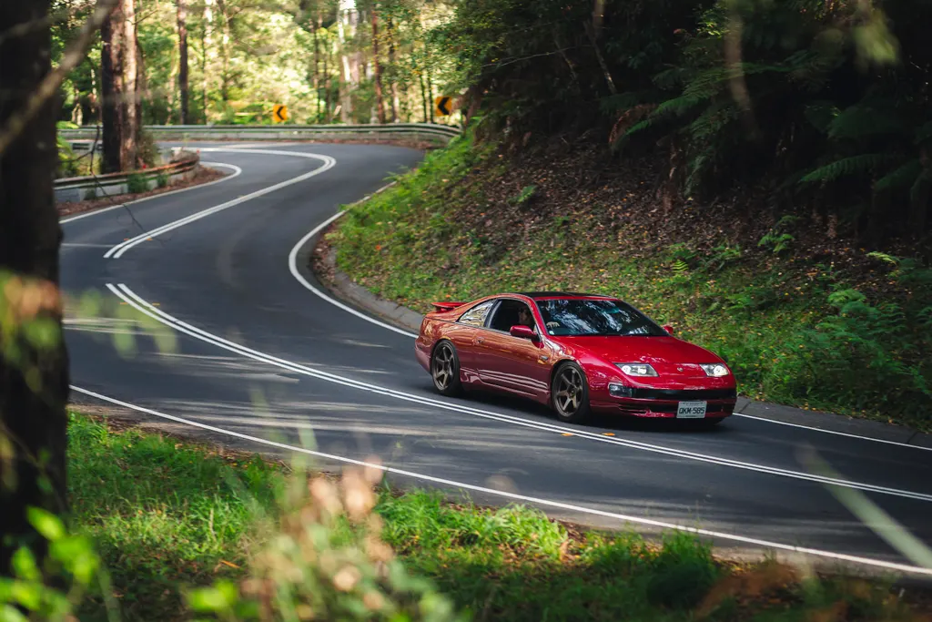 Red sports car navigating a winding forest road with white center line markings.