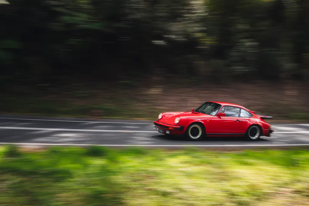 Red sports car driving on a road with blurred forest background captured with motion panning.