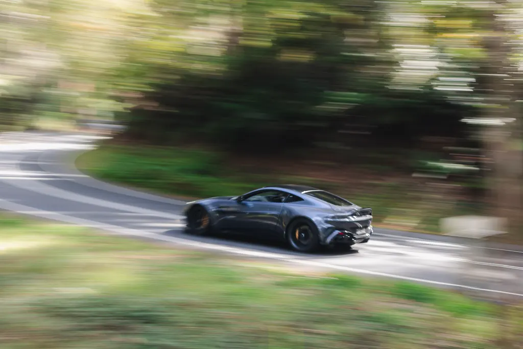 Dark sports car driving on a winding road through dense green forest with motion blur effect.