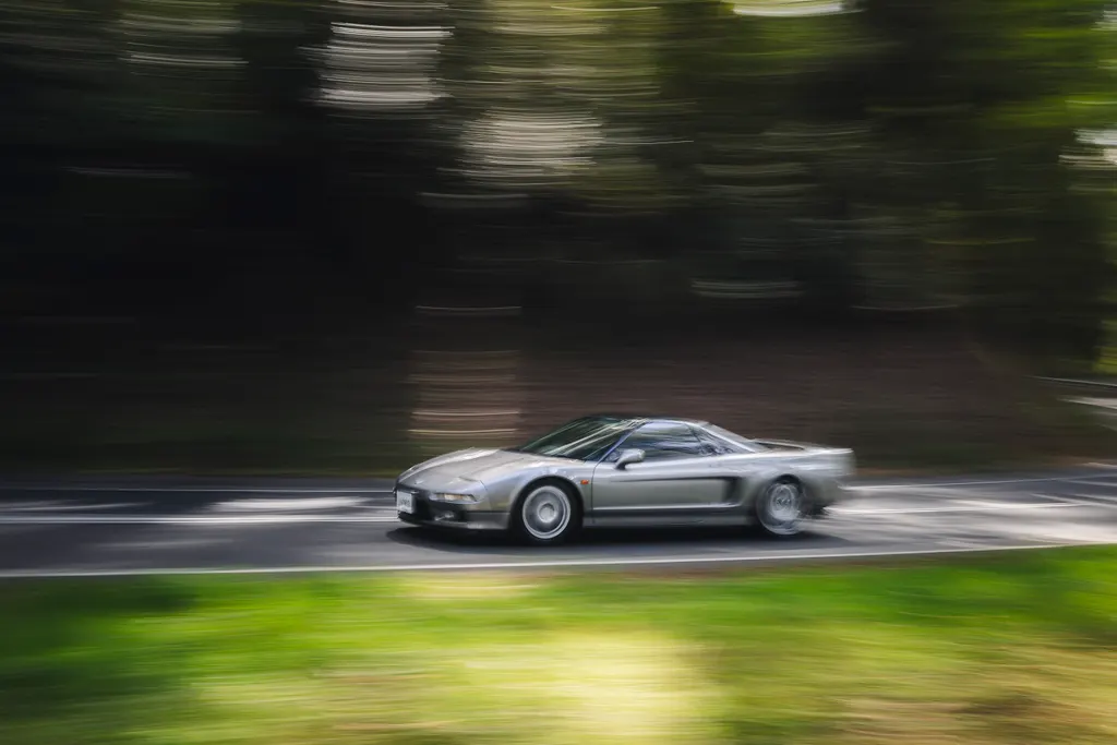 Silver sports car in motion on a tree-lined road with motion blur effect.