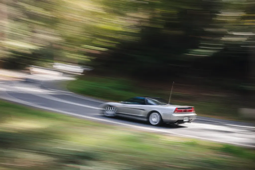 Silver convertible driving on a wooded road with motion blur effect.