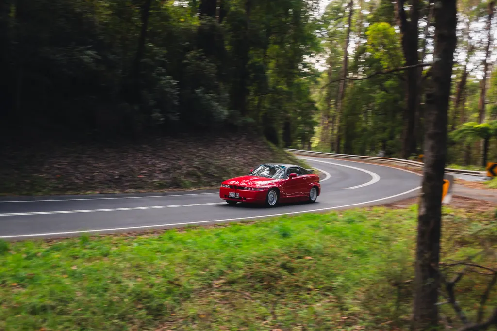 Red sports car on a curved forest road with motion blur effect.