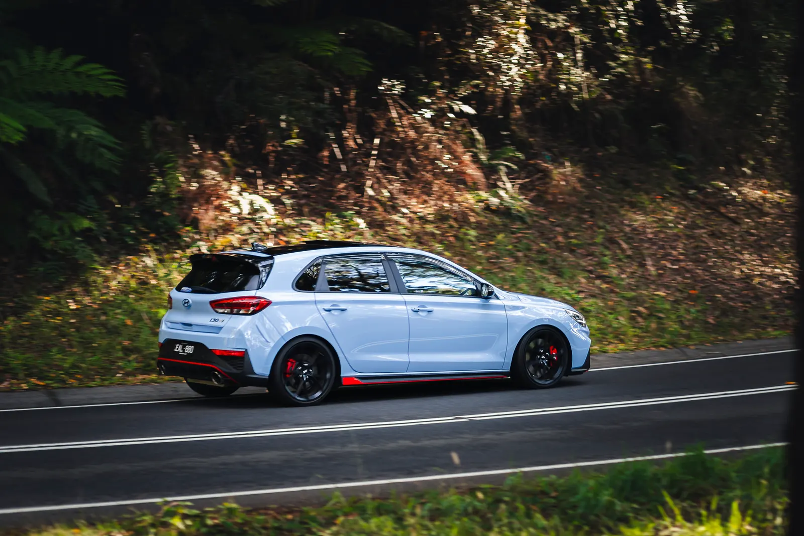 White hatchback with red accents driving on a tree-lined road.