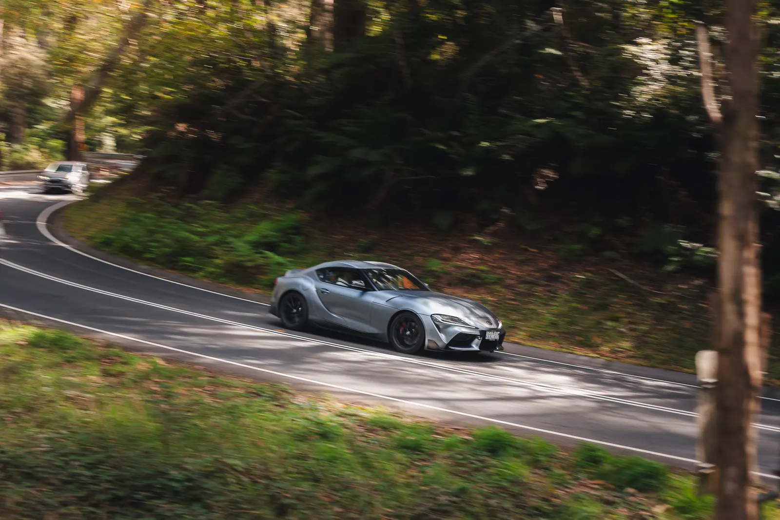 Silver sports car cornering on a wooded road with motion blur surrounding the vehicle.