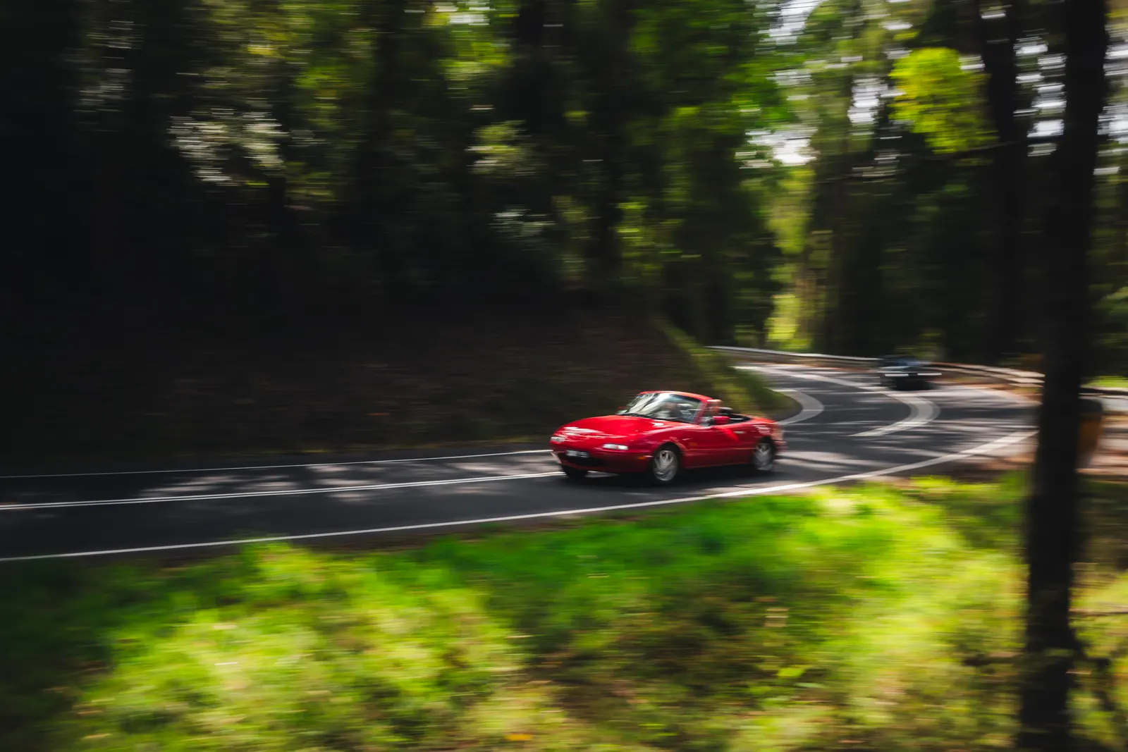 A red sports car driving on a winding forest road with motion blur in the trees.