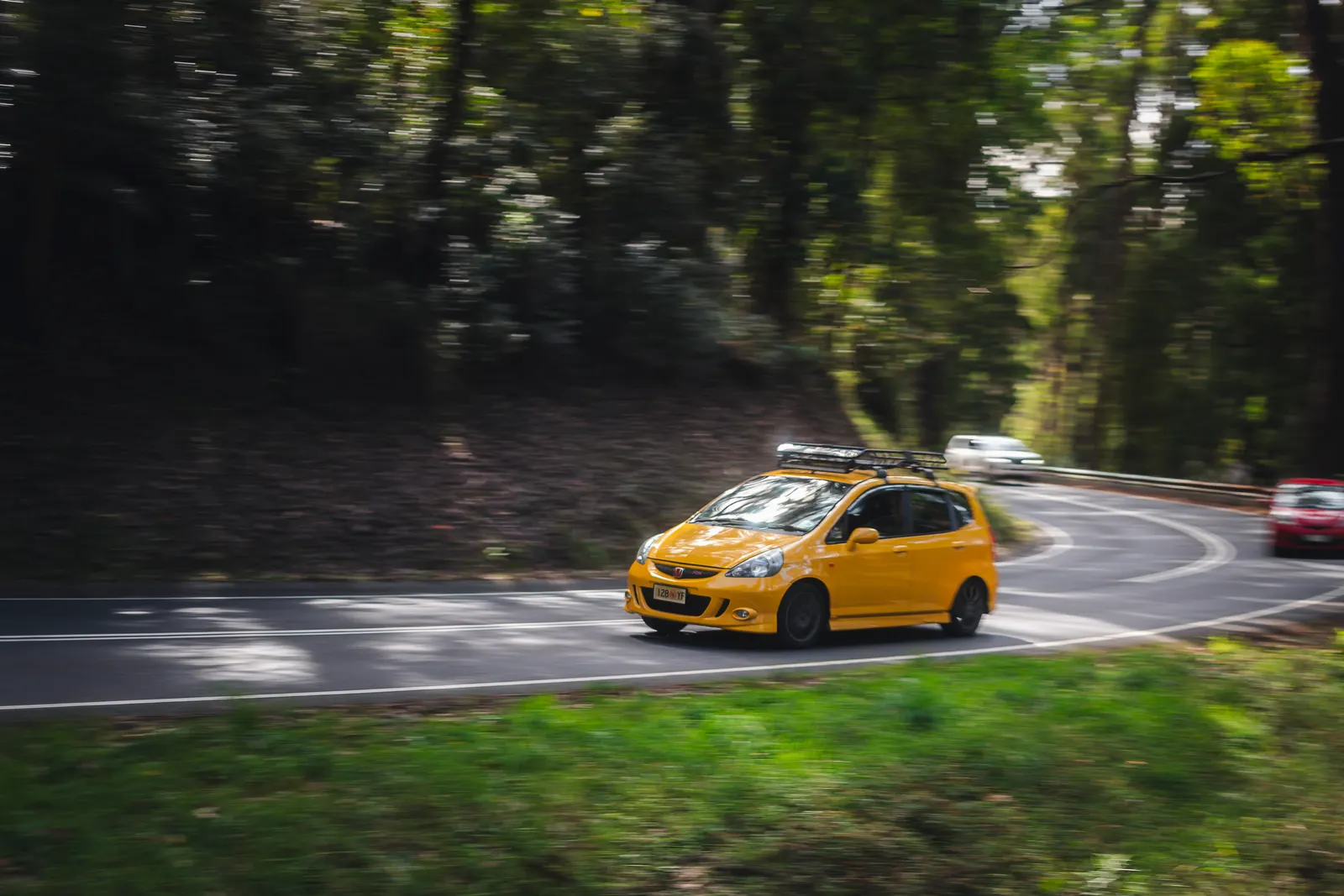 Yellow hatchback navigating a forest road curve with motion blur surrounding foliage.
